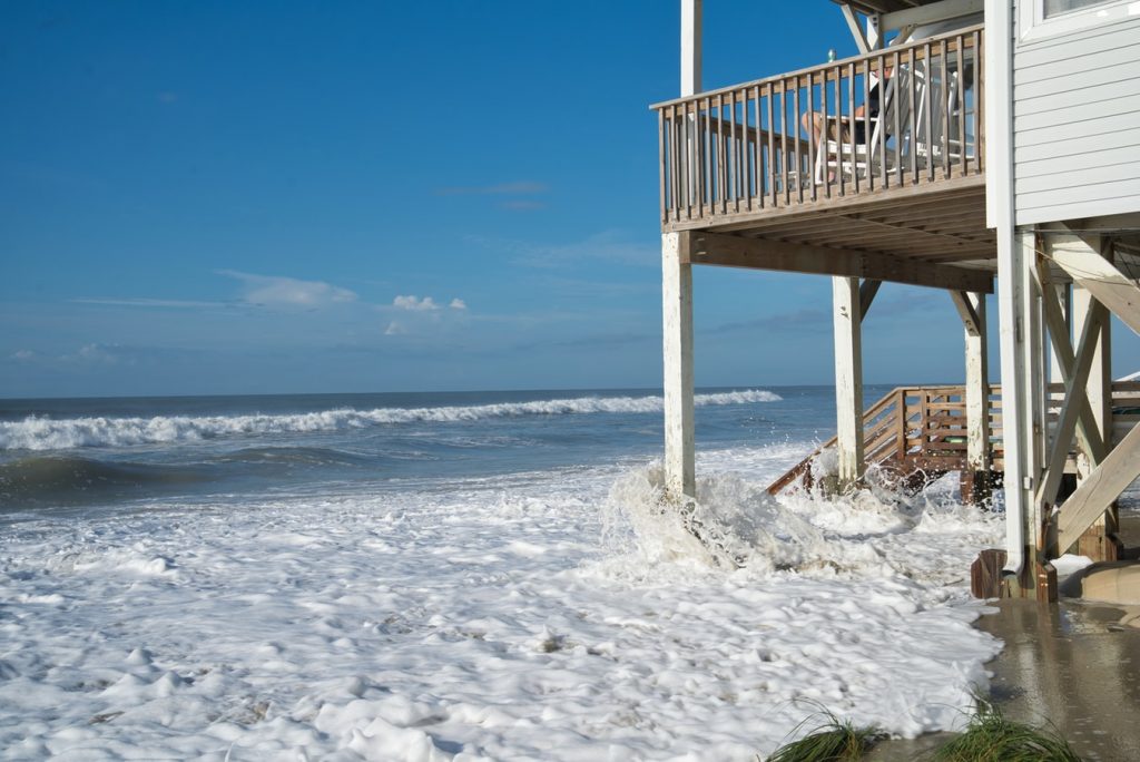 Image of a house with ocean waves splashing under it meant to represent rising sea levels caused by climate changing. Photo by Clint Patterson via Unsplash