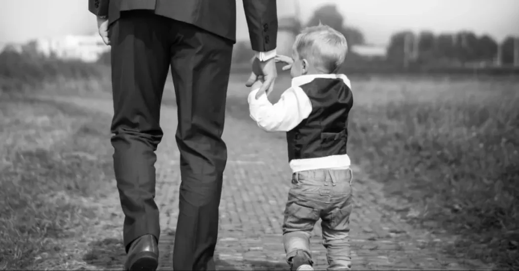 Image of a father and son holding hands walking along a brick paved path toward a house in the distance.