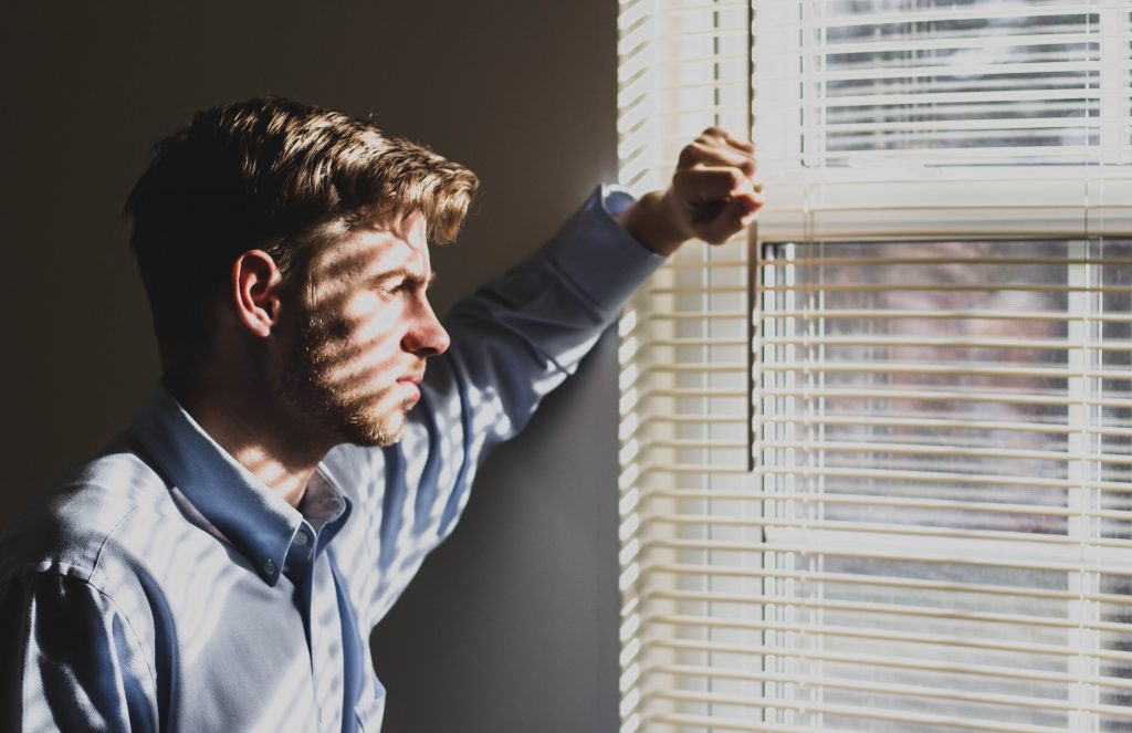 Person standing, looking out a window contemplating how they are unable to pay their mortgage.