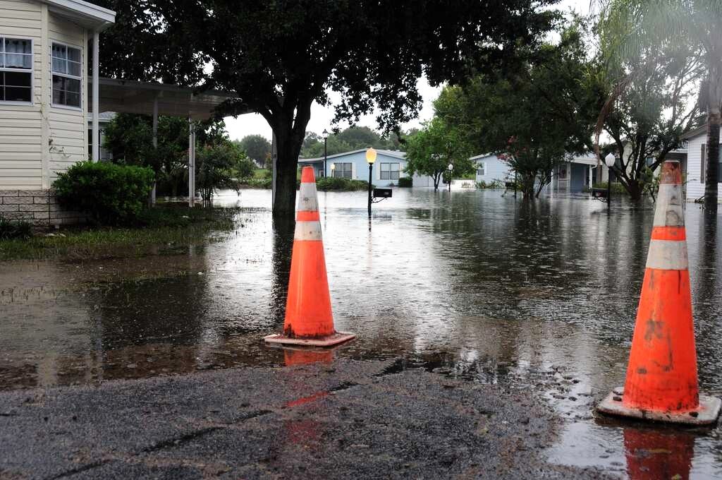Image of a water flooded neighborhood with orange cones marking the water line danger. Captioned: How Emergencies Impact Titles & Mortgages
