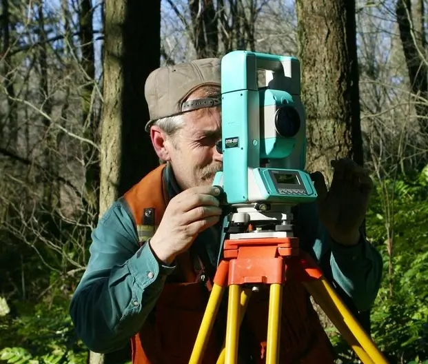Image of a person in the woods using survey equipment to do a property survey.