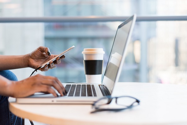Image of a person using a laptop computer and a smart phone at the same time. Captioned: Black Homeownership and Housing: Amid Persistent Discrimination, New Potential for Change