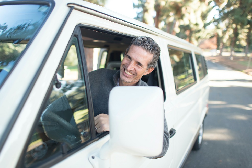 Image of a person with a big smile driving a van on a street on a sunny day. Captioned: A Gig Worker's Guide to Home Buying