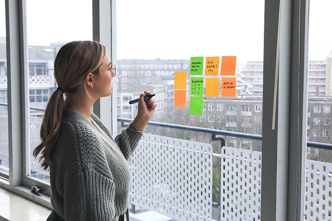 Image of a person with a marker in their hand looking out a window with sticky notes on it. Captioned: Unemployment and the Hopeful Home Buyer