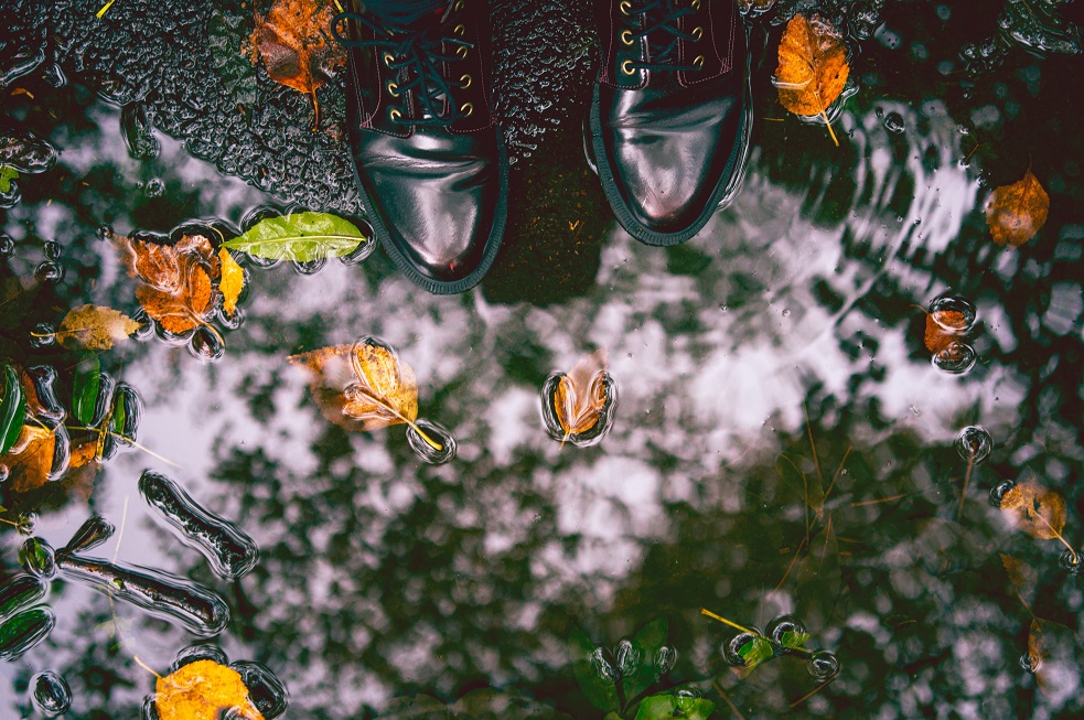 Image of someone's feet next to a puddle of water with leaves in it. Captioned: Inundated, The National Flood Insurance System