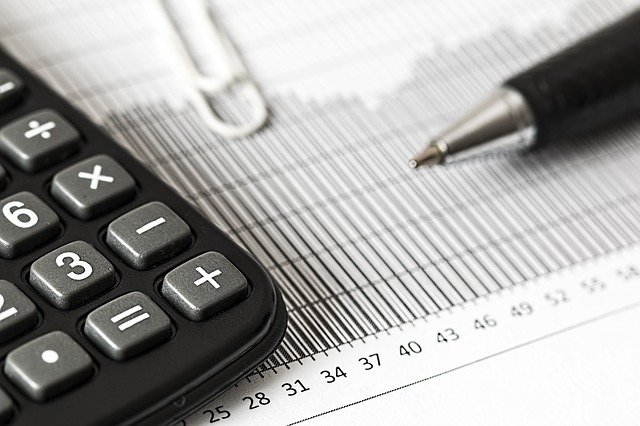 Black and white image of a calculator, a paperclip, and a pen sitting on a paper ledger used for accounting. Captioned: Is a Quitclaim Deed Subject to Tax?