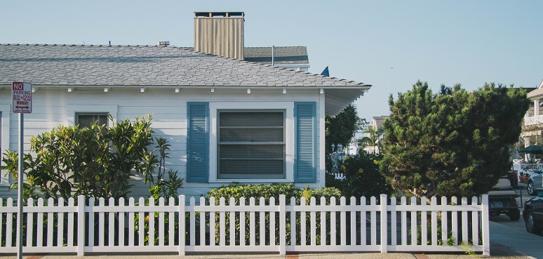 Image of the outside of a house in a city. It has a white picket fence and nice landscaping. Captioned: What Is a Short Sale — And What Does It Mean for Home Buyers?