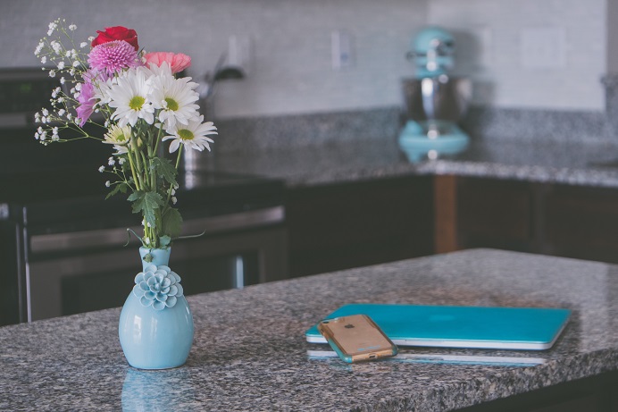 Image of a kitchen counter with a laptop computer, a cell phone, and a vase full of flowers. Captioned: Condos and Co-Ops: The Reputation Management Challenge