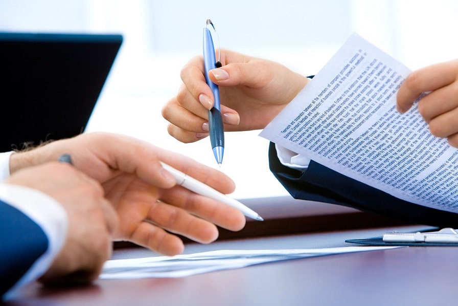Image of people reviewing legal documents with pens in their hands. Captioned: How Does a Limited Warranty Deed Work?