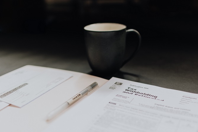 Image of a coffee cup and a pen sitting on tax forms. Captioned: Paying Taxes as the Owner of an LLC