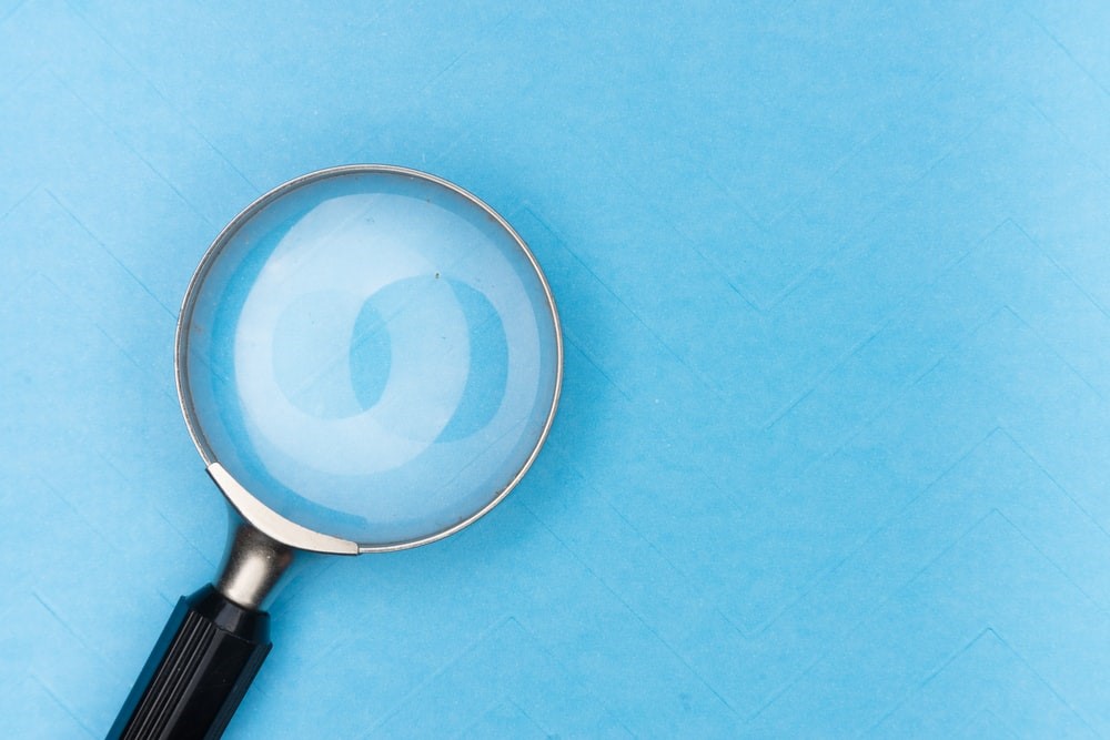 Image of a magnifying glass laying on a blue background. Captioned: Frequently Asked Title Search Questions