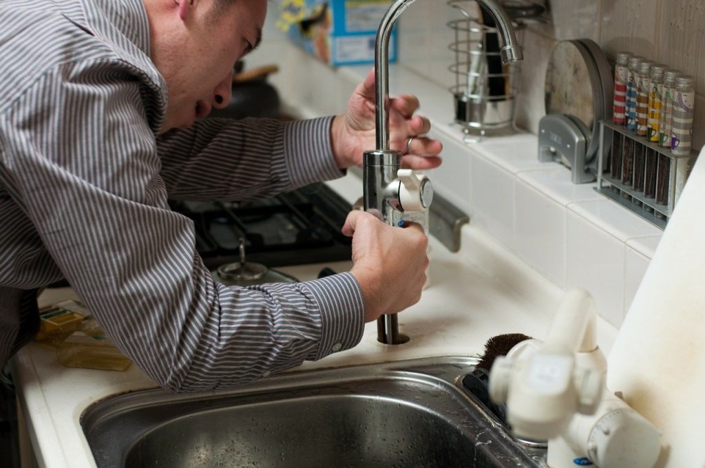 Image of a person, likely a plumber, working on a kitchen sink.