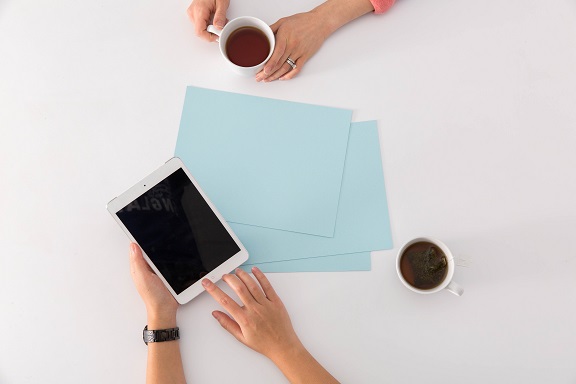 Image of some paper, a couple of cups of coffee, and hands using a tablet computer. Captioned: Hot Tips for Tax Season — And for Hopeful Homeowners
