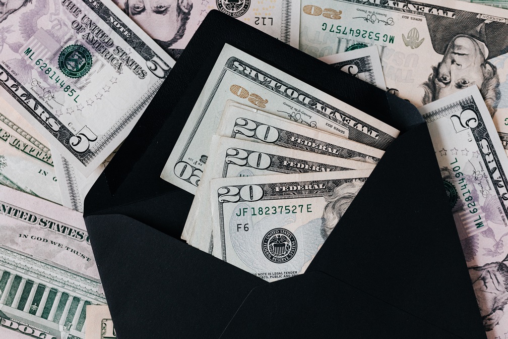 Image of paper currency, money, laying on a table with some in an envelope. Captioned: How Escrow Helps Home Buyers—And When It Hurts