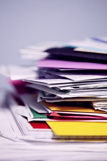 A blurry stack of documents, papers, and folders with many different colors. Captioned: The Case for Paying Tax and Insurance Bills Yourself, Rather Than Through Escrow