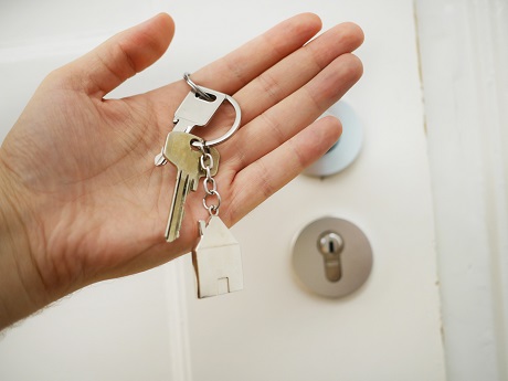 Picture of a person's hand holding a set of house keys in front of the front door to a house. Captioned: How Can the Seller Offset Profits and Reduce Taxable Gains?