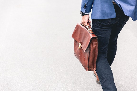 Image of a person with a leather briefcase walking away from the camera. Captioned: How Much Will You Pay Your Real Estate Agent?