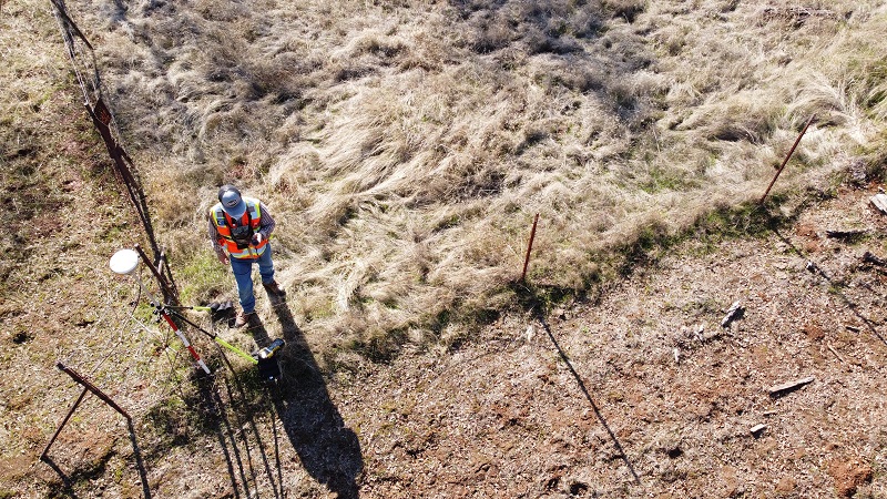 Image of a surveyor inspecting property line on a piece of real estate outside.