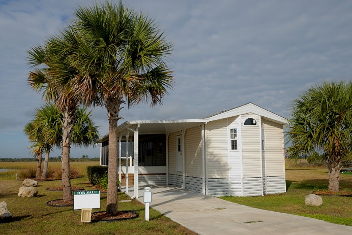 Mobile home exterior with a driveway and palm trees. Captioned: Convert a Mobile Home Title to a Real Estate Title