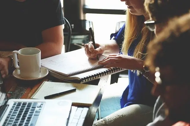 Image of a group of people working on documents at a table in a coffee shop type setting.