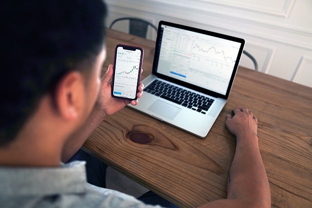 Person looking at a cell phone and a computer while sitting at a desk. Captioned: The Rise of the Outside-the-Box Mortgage Applicant