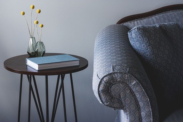 Image of a chair and end table with a book and small flowers.