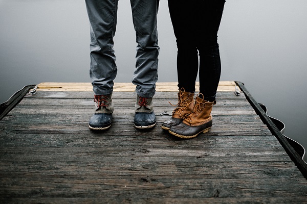 Image of the legs of two people standing on a dock near a body of water.