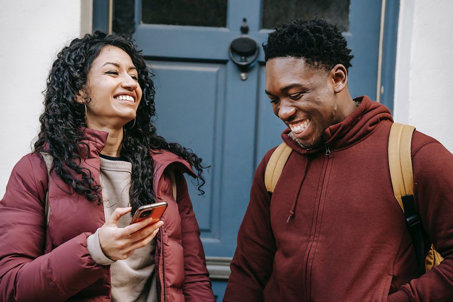 A couple of people standing outside a house looking at a real estate app on their phone.