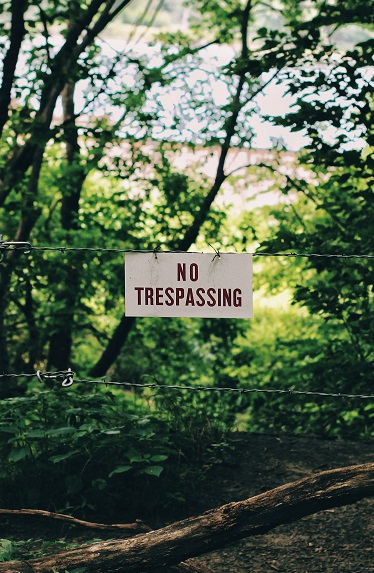Image of a no trespassing sign hanging on a wire fence in the woods. Captioned: How Do Boundaries Become Disputed?