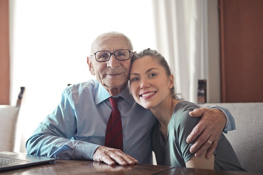 Two people sitting at a desk hugging and smiling.