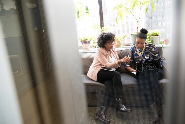 Two people sitting on a gray couch looking at a computer and paperwork reviewing a real estate appraisal.