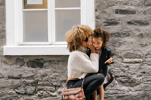 Image of an adult whispering to a child outside of a house.