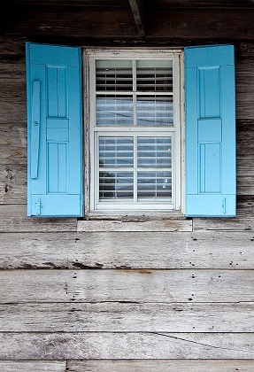 Image of a house window with blue shutters and weathered wood siding.
