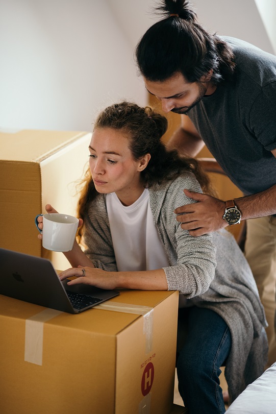 Two people looking at a computer surrounded by moving boxes.