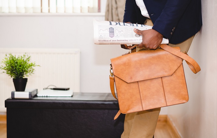 Person walking into a house carrying a newspaper and a soft briefcase.