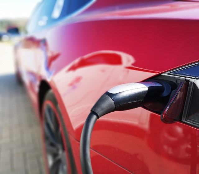 Out of focus image of an electric car with the charging cord plugged in.