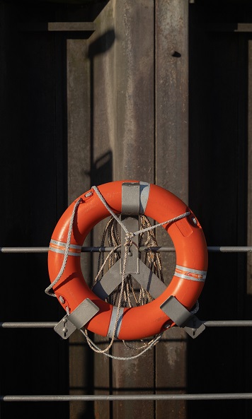 Image of an orange, round floatation device secured with rope to a waterside dock railing.
