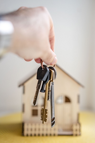Image of a hand holding a set of keys in front of a small model home.
