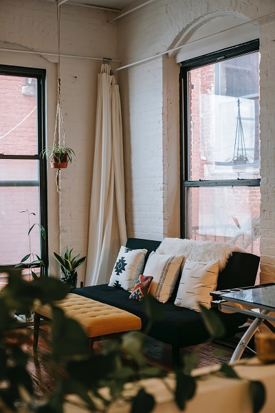 Cluttered interior of an older looking condo or apartment, exposed brick walls, urban city scape views out of the windows.