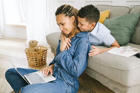 Parent and child sitting on a couch looking at a computer in a cozy looking house.