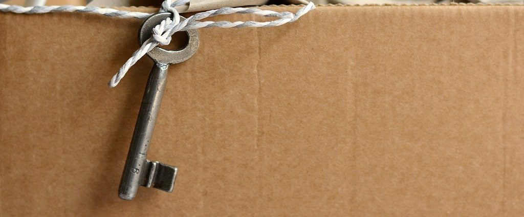 Image of an old looking skeleton key tied to string resting upon a cardboard box.