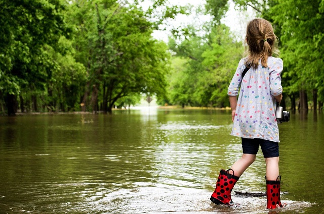 A young person in rain boots walking in shallow water.