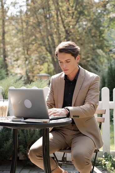 Person, outside at a table, working on a laptop computer. Captioned: Mortgage Borrowers Warm Up to RON’s Anti-Fraud Safeguards