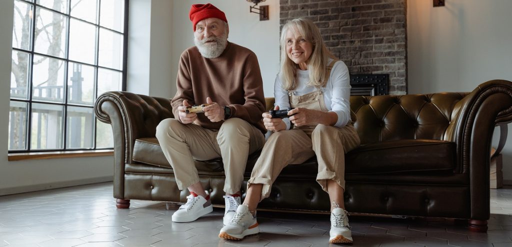Two people sitting on a brown couch in a sparsely furnished house playing video games. They should probably get a job.