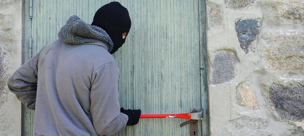 Person dressed as a burglar trying to open a house door with a crow bar.