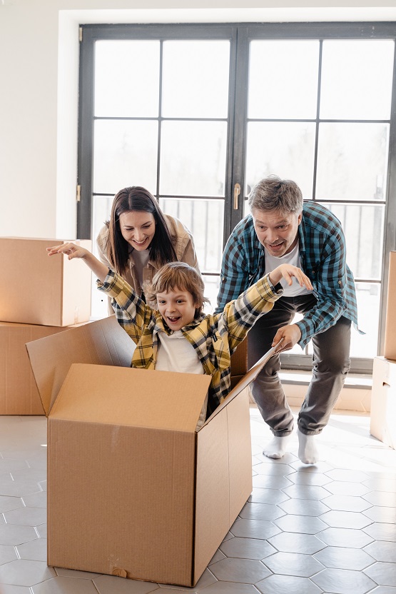 Two adults and a child playing in an empty moving box after moving into a new home.