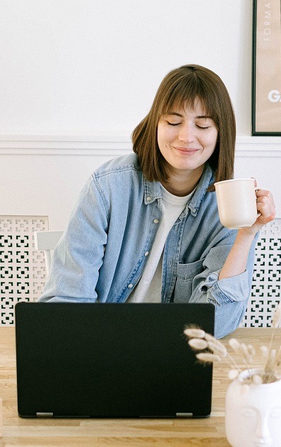 Person using a laptop computer and drinking coffee seemingly happy.