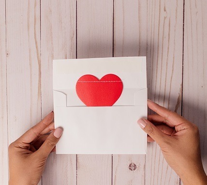 Person holding an open envelope and letter with a red paper heart attached to the letter.