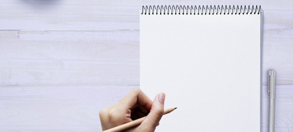 Image of a person holding a pencil ready to write on a blank paper tablet.