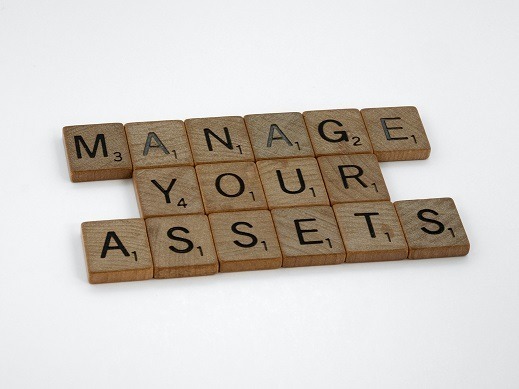 Wood letter tiles arranged to form the words "Manage Your Assets"